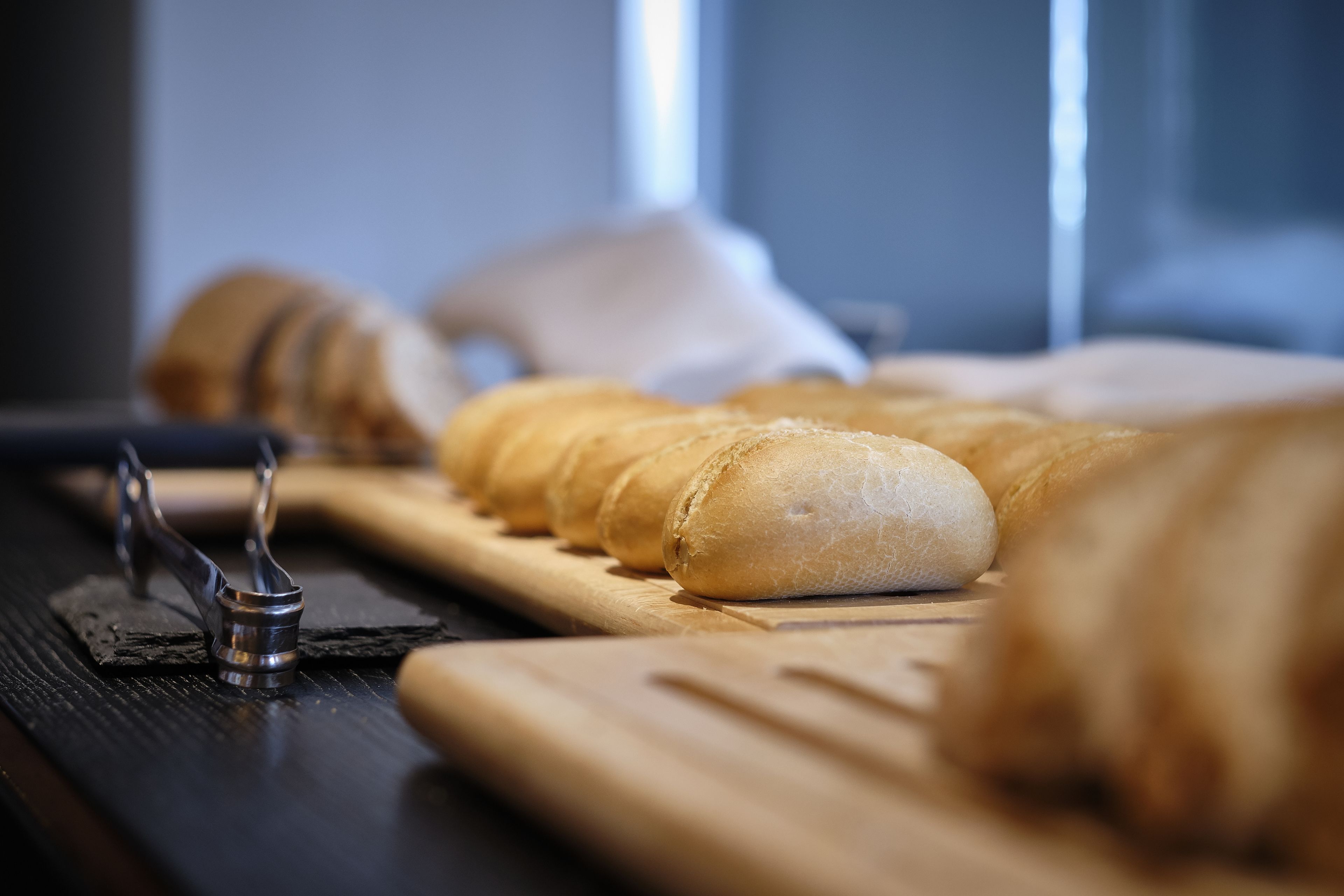 A wooden cutting board with several loaves of bread and a bread slicer.