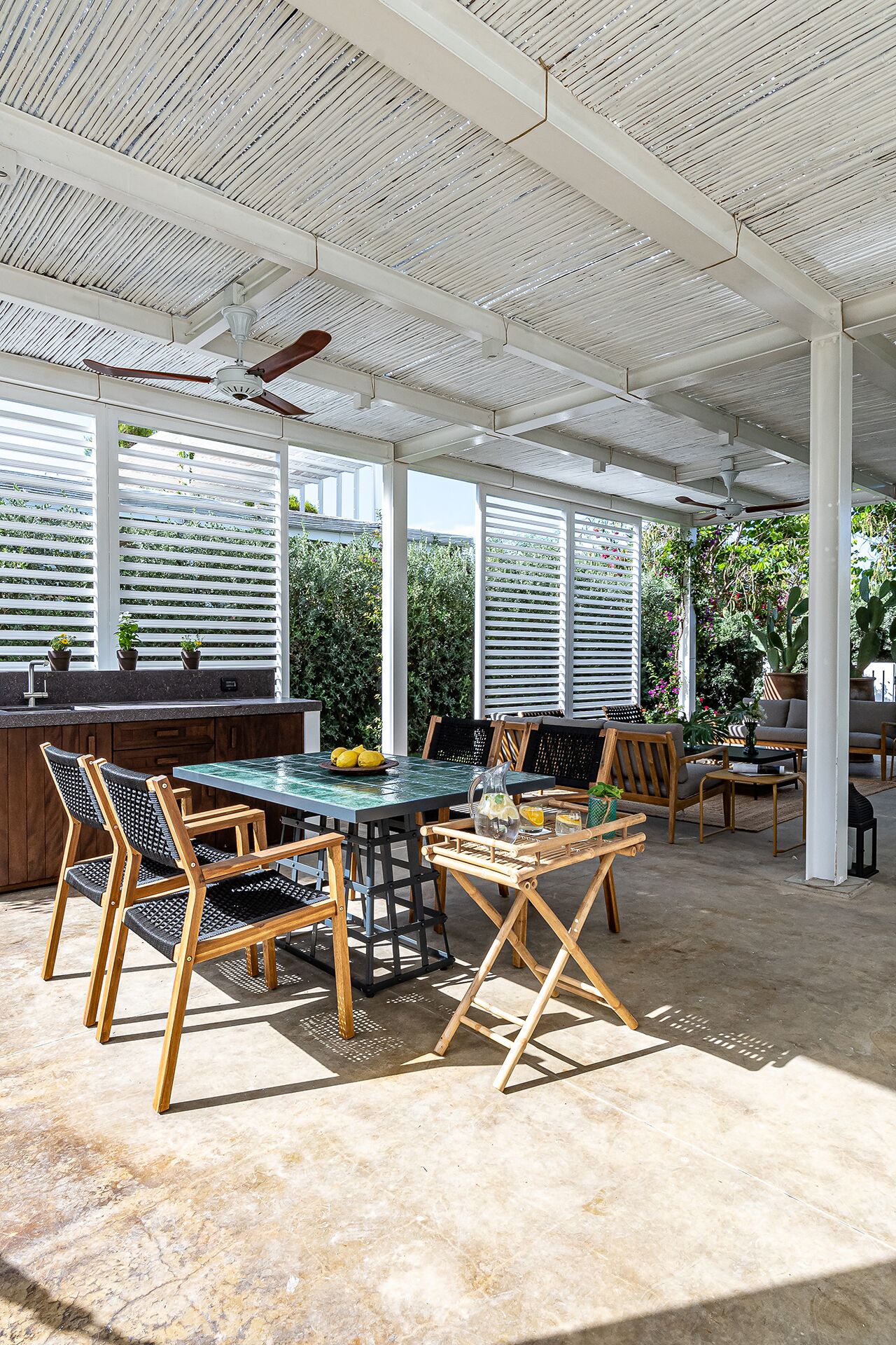 An outdoor patio with a table and chairs, a ceiling fan, and a view of greenery.
