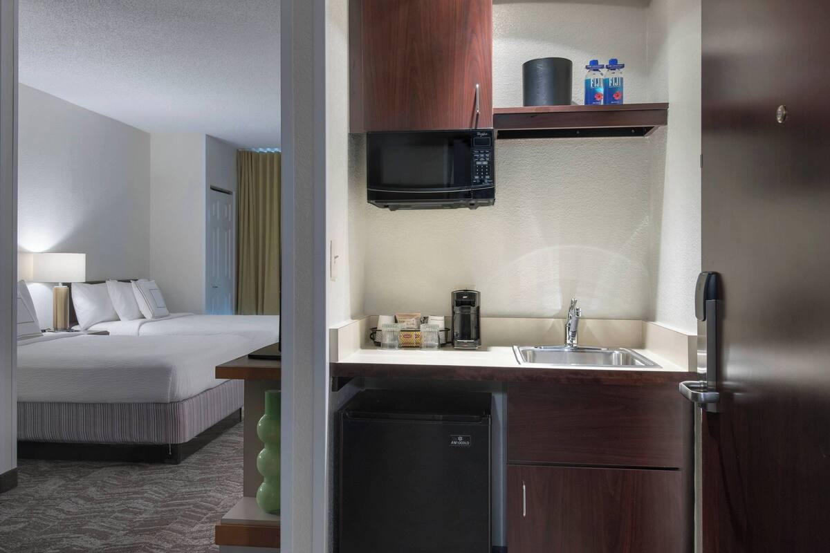 A hotel room with a bed, a small kitchenette with a microwave, a coffee maker, and a mini fridge.
