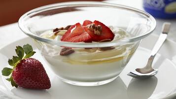 A dessert in a clear glass bowl on a white plate, accompanied by a spoon and a strawberry.