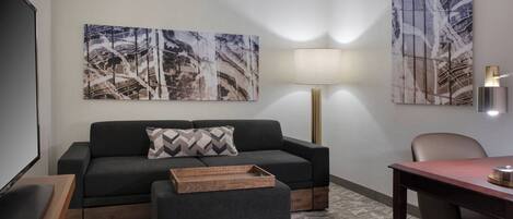 Una sala de estar moderna con un sofá, un reposapiés y una mesa de comedor. Hay dos grandes cuadros abstractos en las paredes y una lámpara de pie.