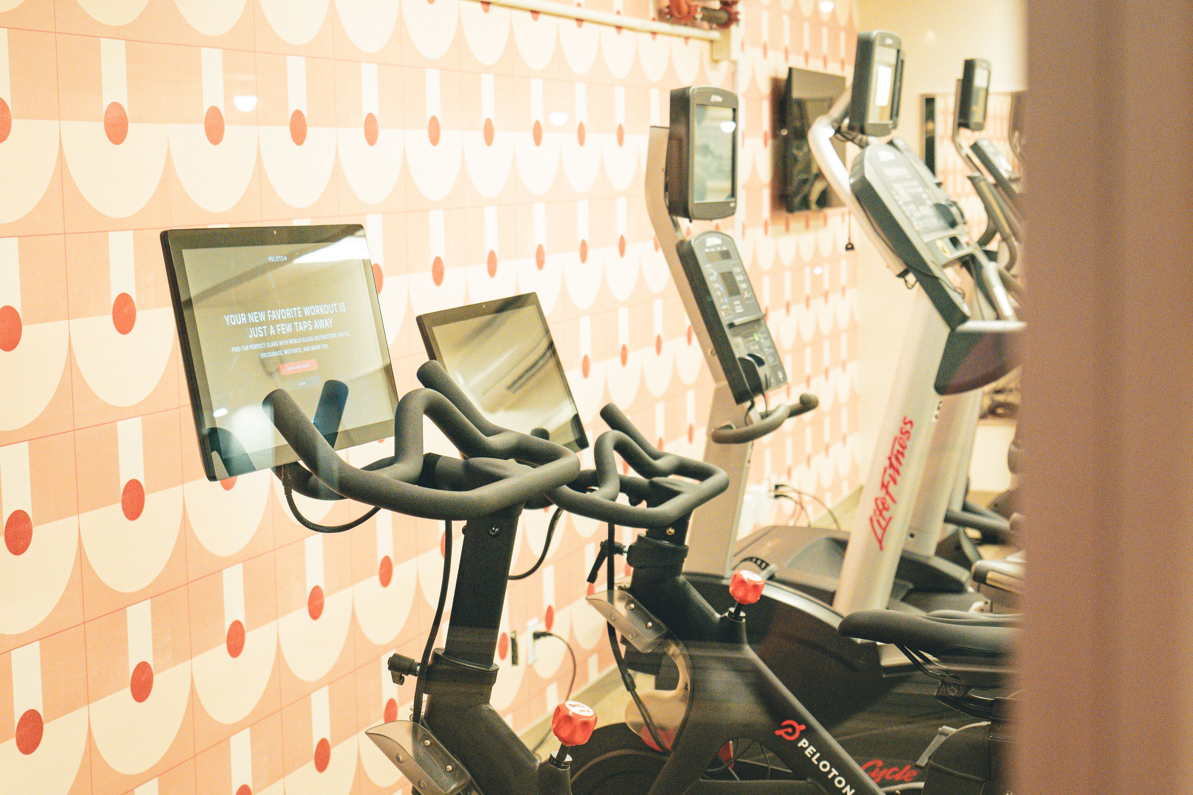 Varias bicicletas estáticas en un gimnasio, con un pared decorada en el fondo.