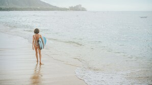 Escena de playa con una persona cargando una tabla de surf.
