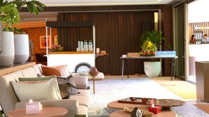Una sala de estar moderna con sofá, mesa de centro y elementos decorativos. En el fondo, se aprecia una zona de cocina con encimera y diversos utensilios.