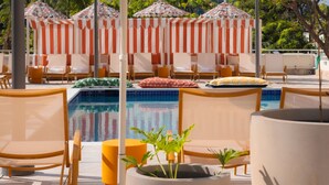 Un área junto a la piscina con sillones de descanso, sombrillas y plantas en macetas.