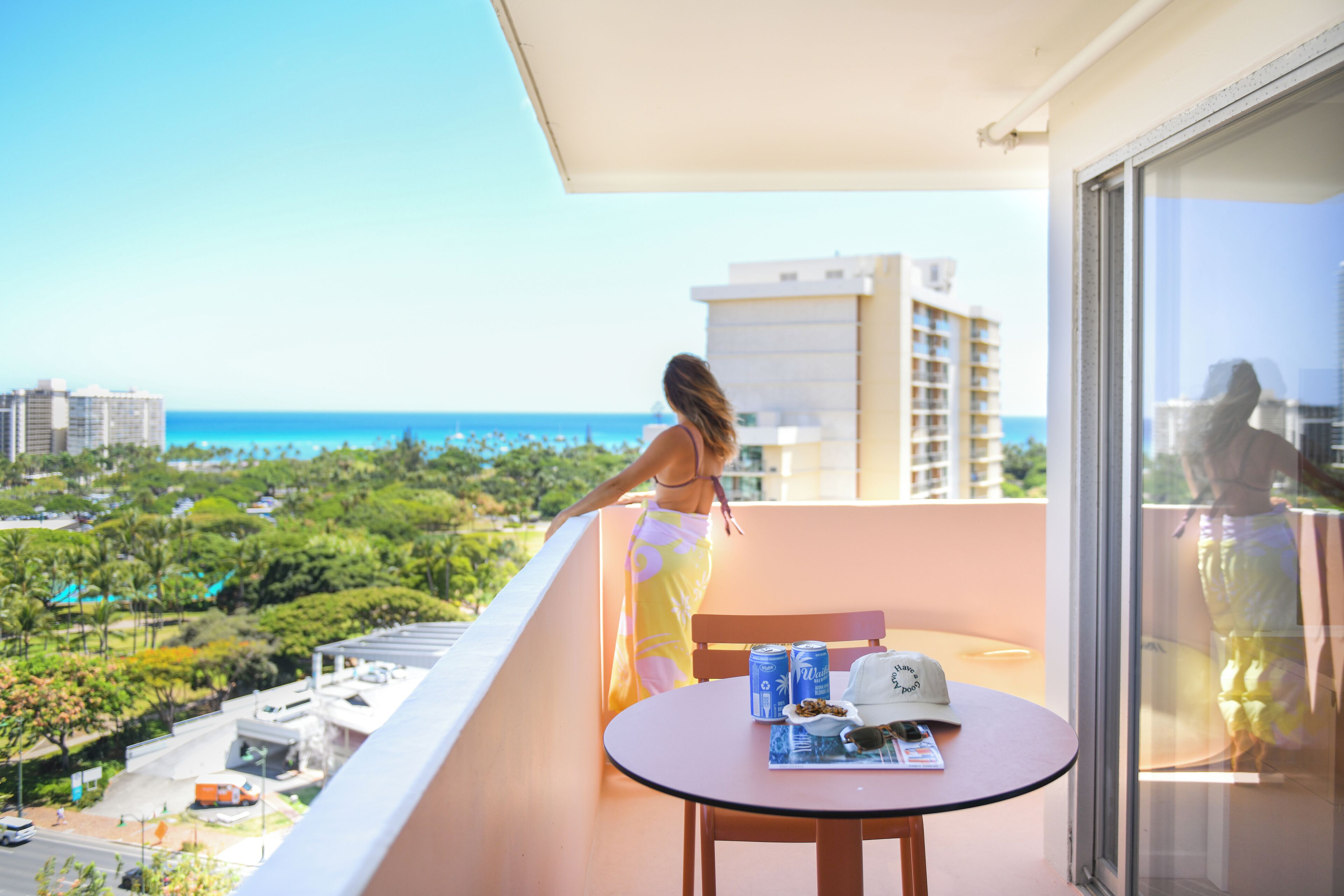 A balcony with a table, a chair, and a view of the ocean and cityscape.