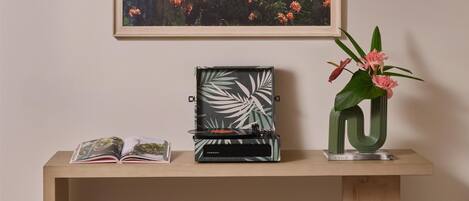 A wooden console table with a framed landscape painting, a vinyl record player, a vase with pink flowers, and a small book titled "Lei Aloha".