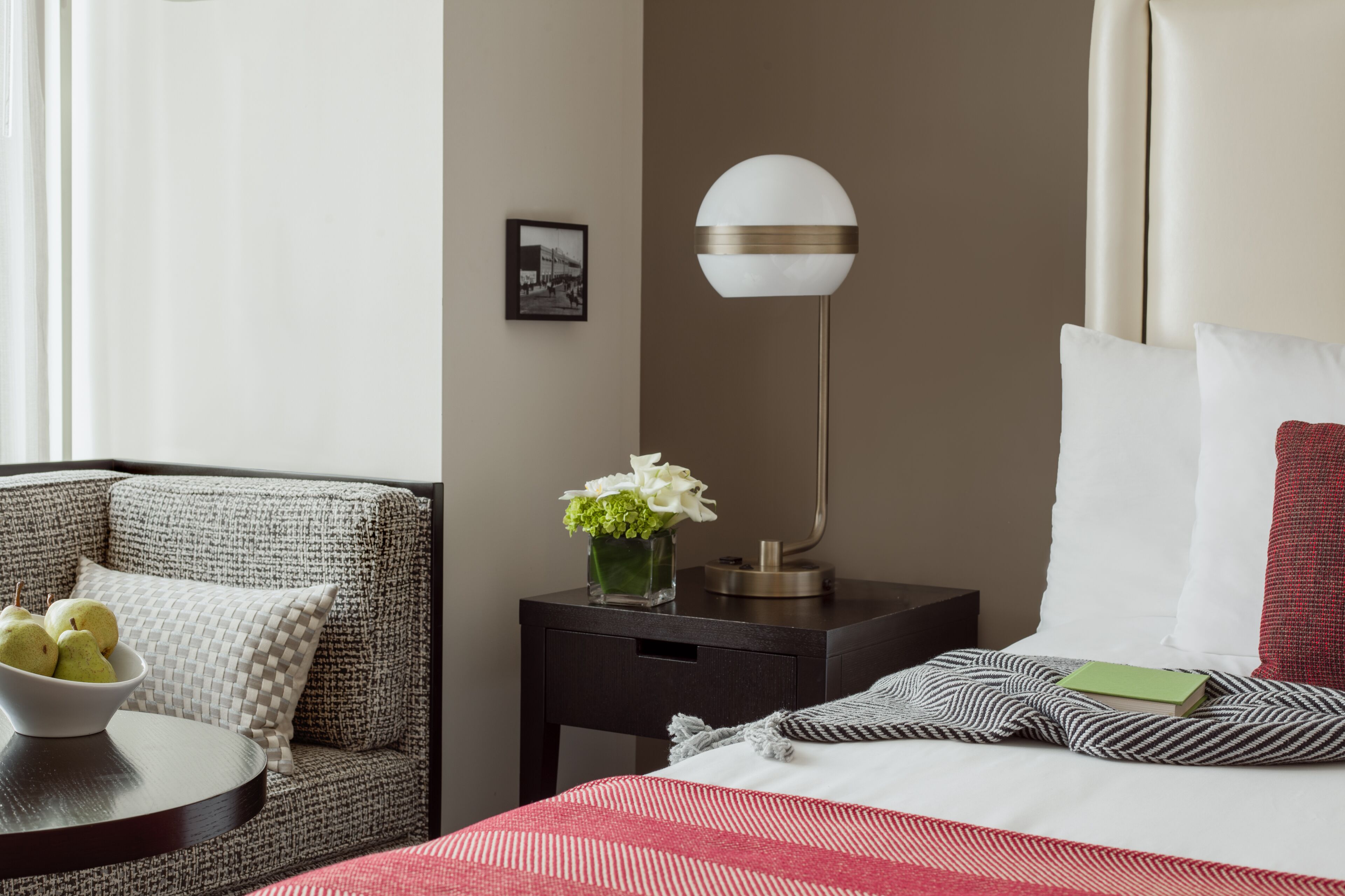 Une chambre d’hôtel avec un lit, une table de chevet, une chaise, une lampe et un tableau au mur.