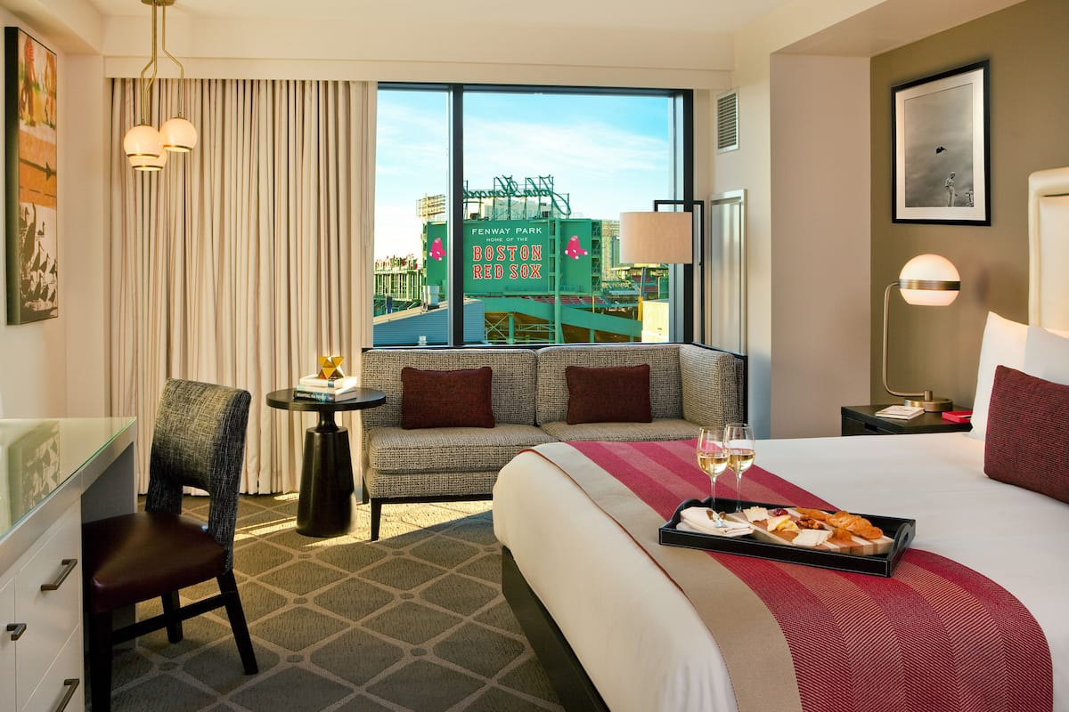 Una habitación de hotel con cama, sofá, escritorio y vistas al Fenway Park.