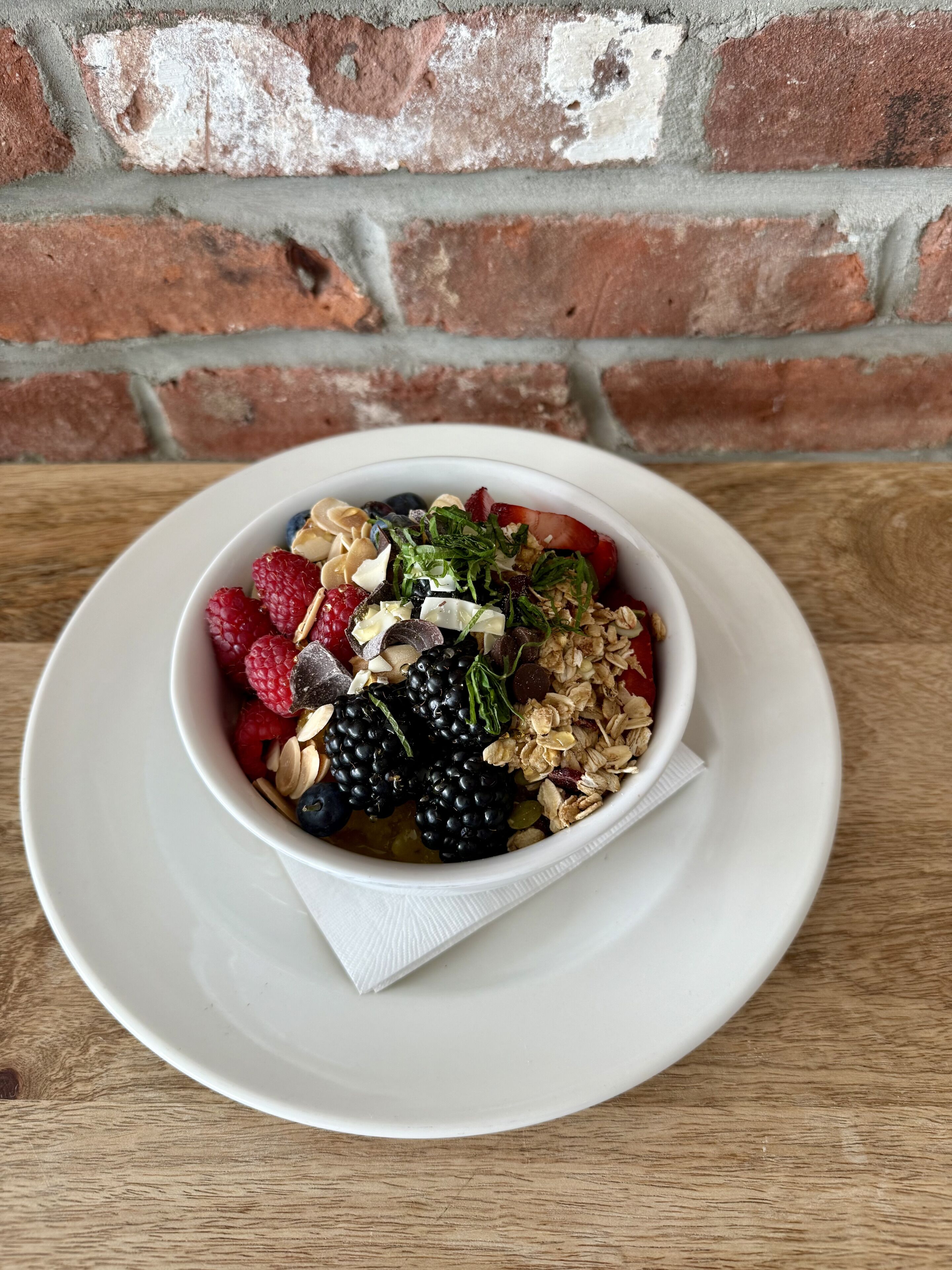 A bowl of mixed berries and nuts on a white plate, placed on a wooden table with a brick wall in the background.
