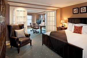 Een hotelkamer met een groot bed, een lederen fauteuil, een bureau met een computer en een televisie.
