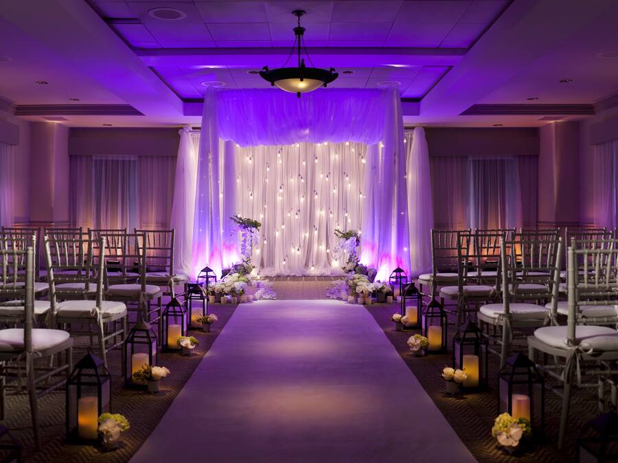 A wedding aisle with chairs on either side, a central aisle, and a backdrop of draped fabric.