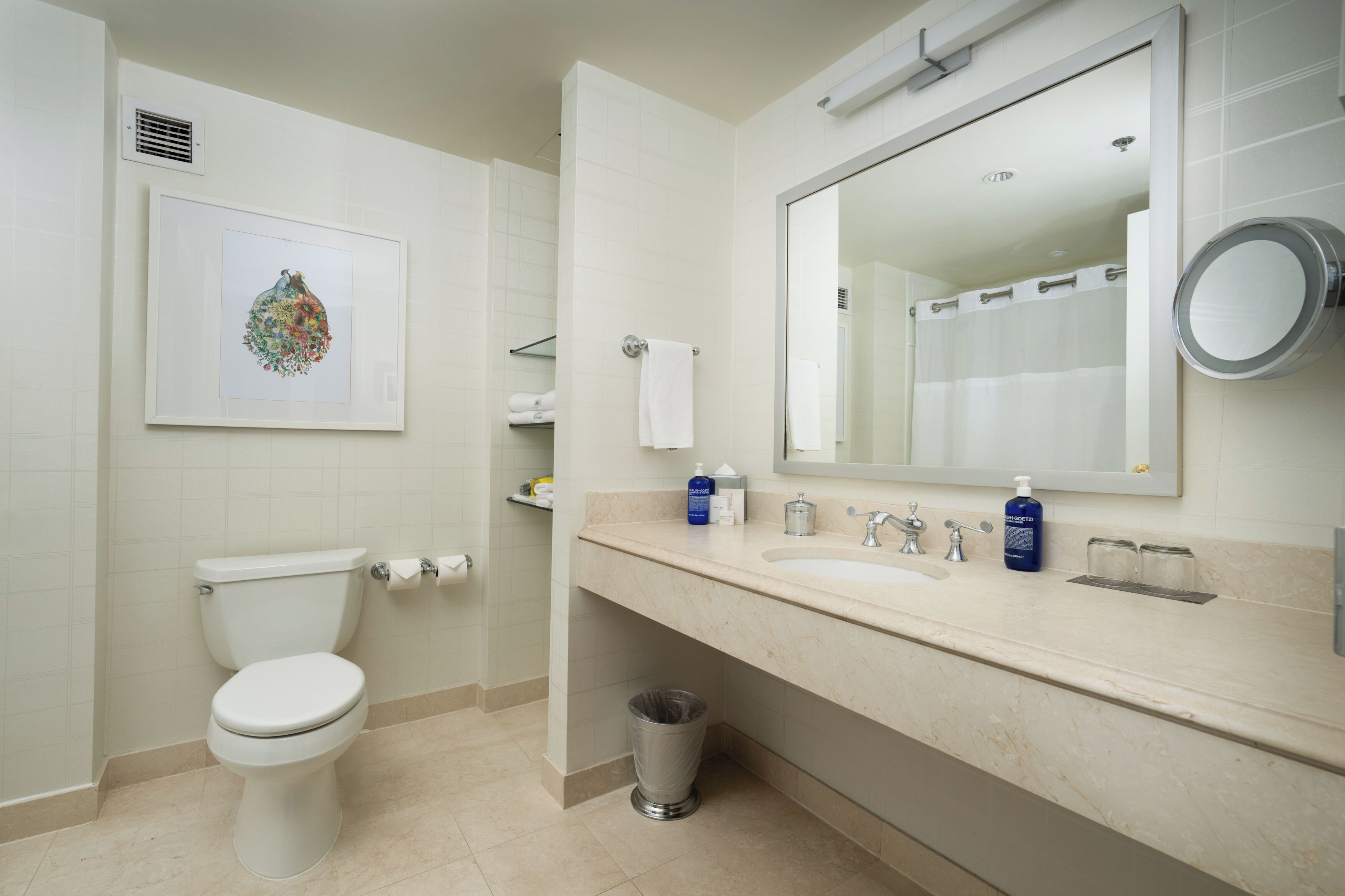 A modern bathroom with a toilet, sink, mirror, and a framed artwork on the wall.