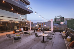 An outdoor seating area with tables and chairs, a bar, and a view of Fenway Park.