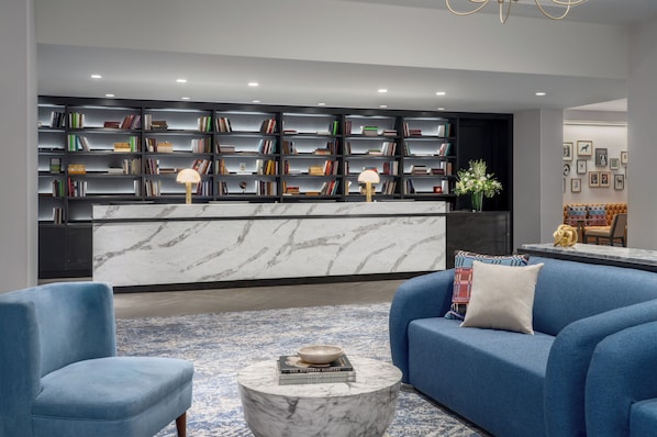 Una sala de estar moderna con un sofá azul, una mesa de centro de mármol y una estantería llena de libros.