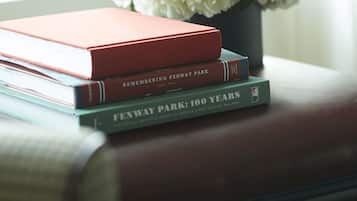 A stack of books on a leather couch with a vase of white flowers in the background.
