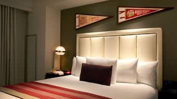 A hotel room with a large bed, a nightstand with a lamp, and two wall-mounted Boston Red Sox pennants.
