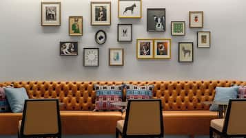 Un salon moderne avec un canapé orange à motifs capitonnés, une table basse et des fauteuils. Des tableaux encadrés sont accrochés au mur, au-dessus du canapé.