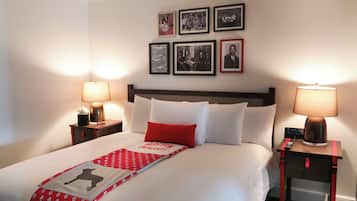 Uma cama bem arrumada com um cobertor vermelho e branco, duas luminárias de mesa e uma série de fotografias emolduradas na parede.