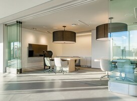 A modern conference room with a glass partition, a round table, and two office chairs.