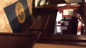 A hotel reception desk with a black and gold logo, a wooden reception counter, and various papers and notices on the wall. - Park Savoy (New York)