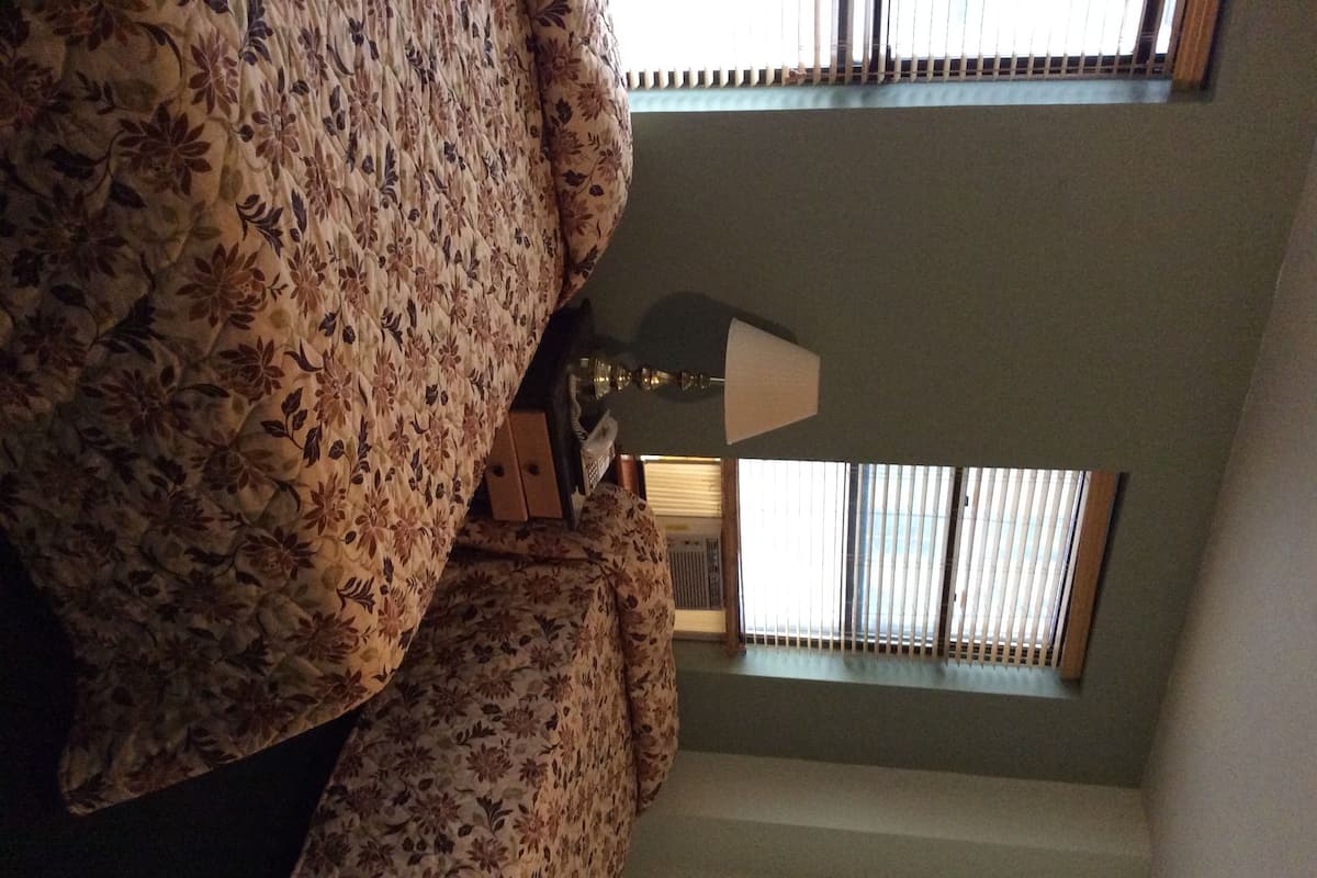 A room with a floral-patterned sofa, a lamp, and a window with blinds.