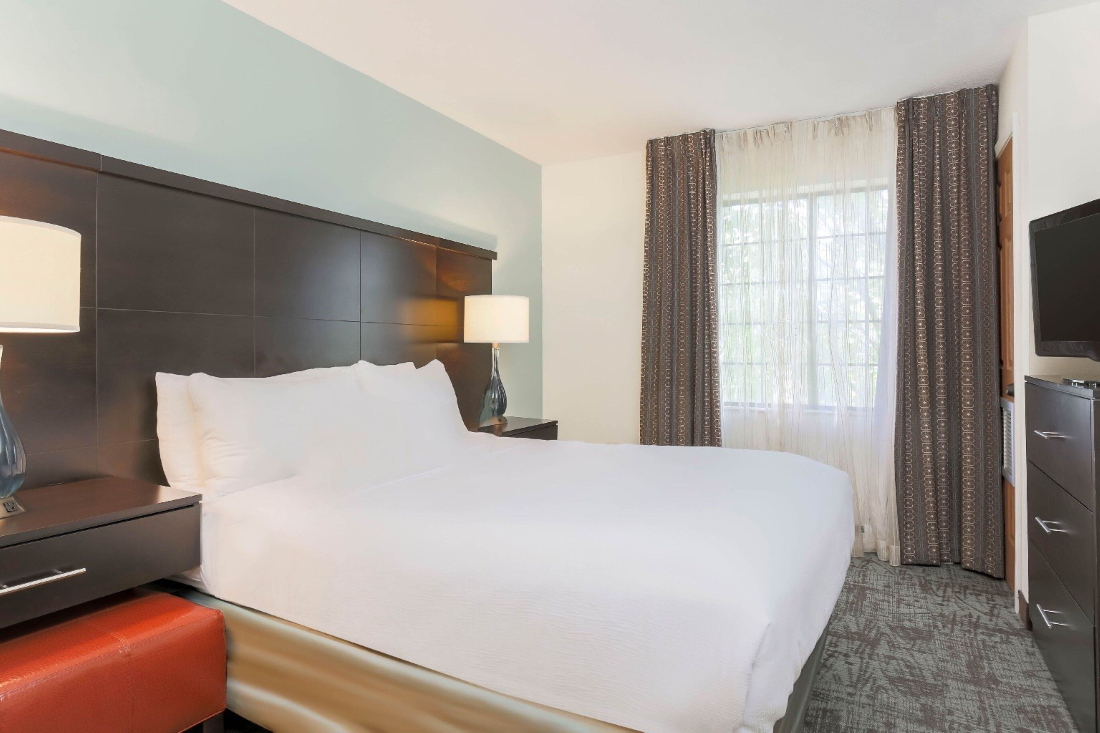 A hotel room with a large bed, a desk with a lamp, a television, and a wardrobe.