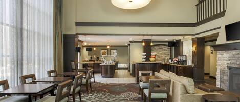 A spacious lobby with a central seating area, a fireplace, and a kitchen in the background.