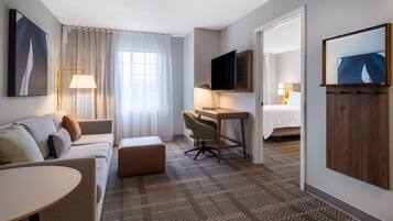 A hotel room with a sofa, a desk, a chair, a TV, and a bed.