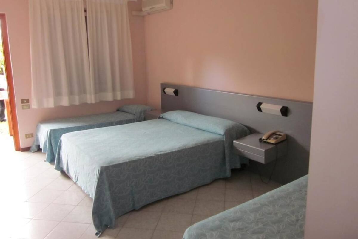 Une chambre d’hôtel avec deux lits, une table de chevet avec un téléphone et une fenêtre avec des rideaux.