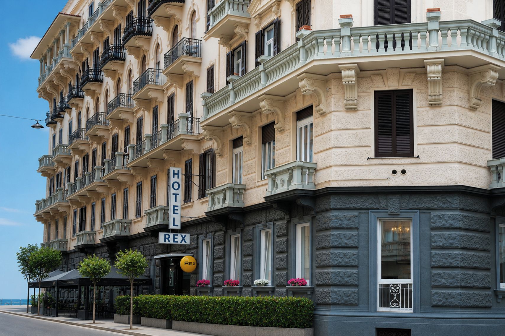 Un hôtel à la façade classique, doté de nombreux balcons et d’une enseigne indiquant le nom « HÔTEL REX ».