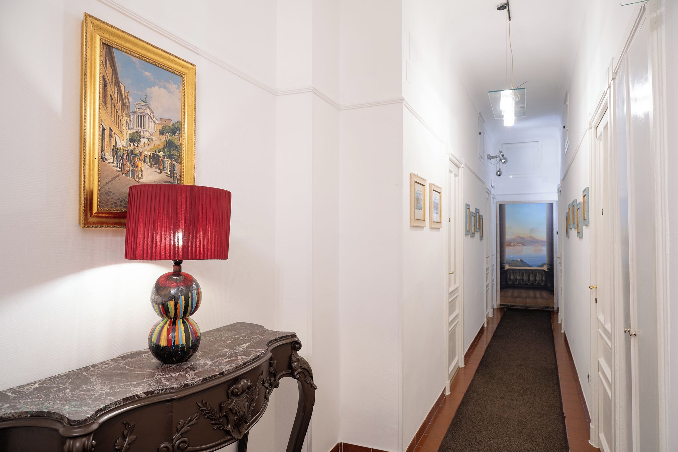 Un couloir avec une lampe, un tableau et une porte donnant sur une autre pièce.