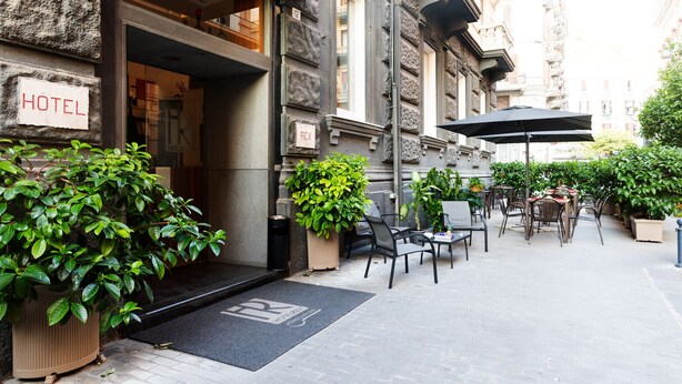Une entrée d’hôtel située à l’extérieur, avec un paillasson, des plantes en pot et des sièges d’extérieur.