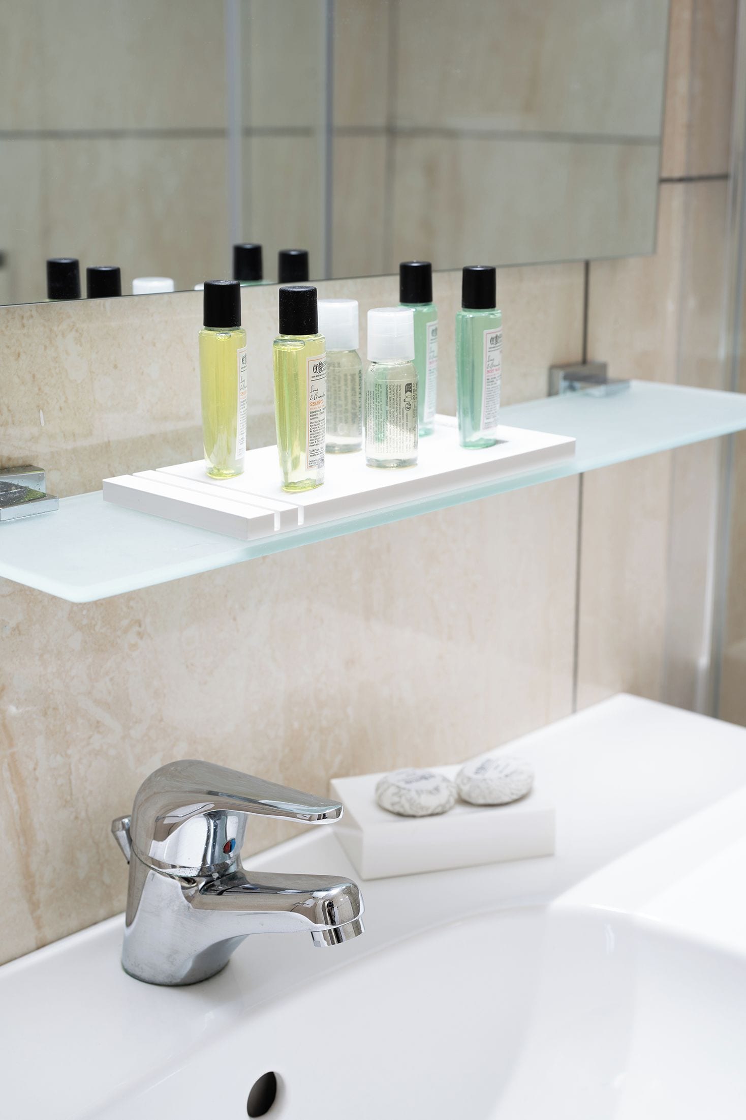 Ein Badezimmer mit einem chromfarbenen Wasserhahn, einer Glasablage mit verschiedenen Pflegeprodukten und einer marmorierten Wand.