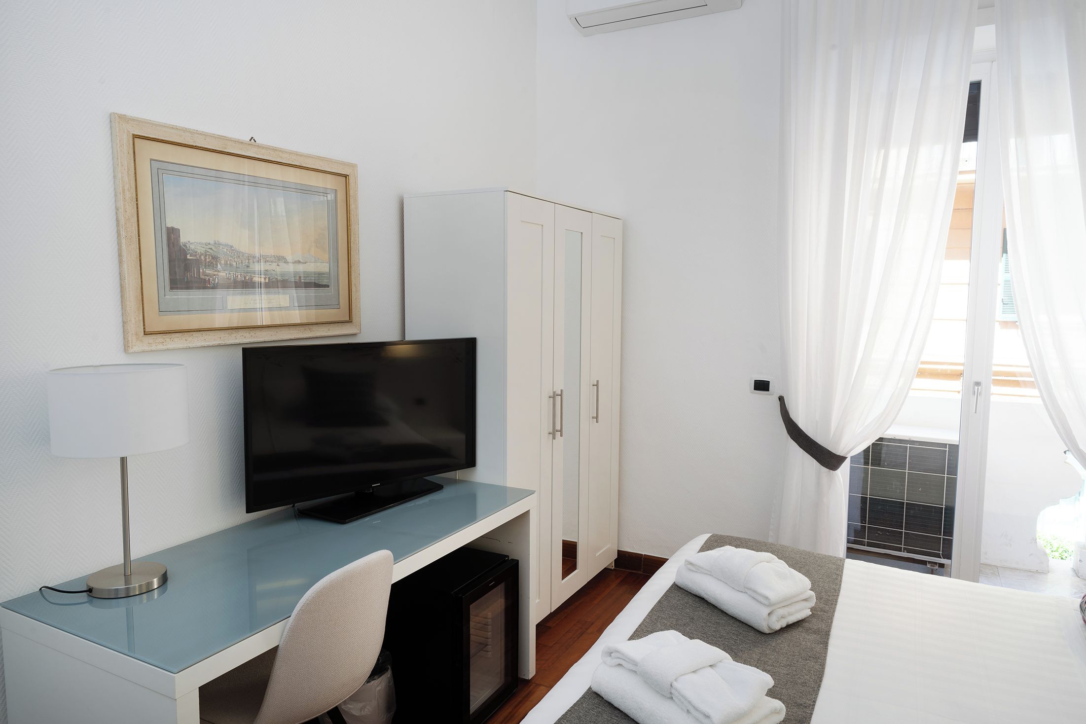 A hotel room with a television on a desk, a cabinet, a bed with a towel, and a window with curtains.