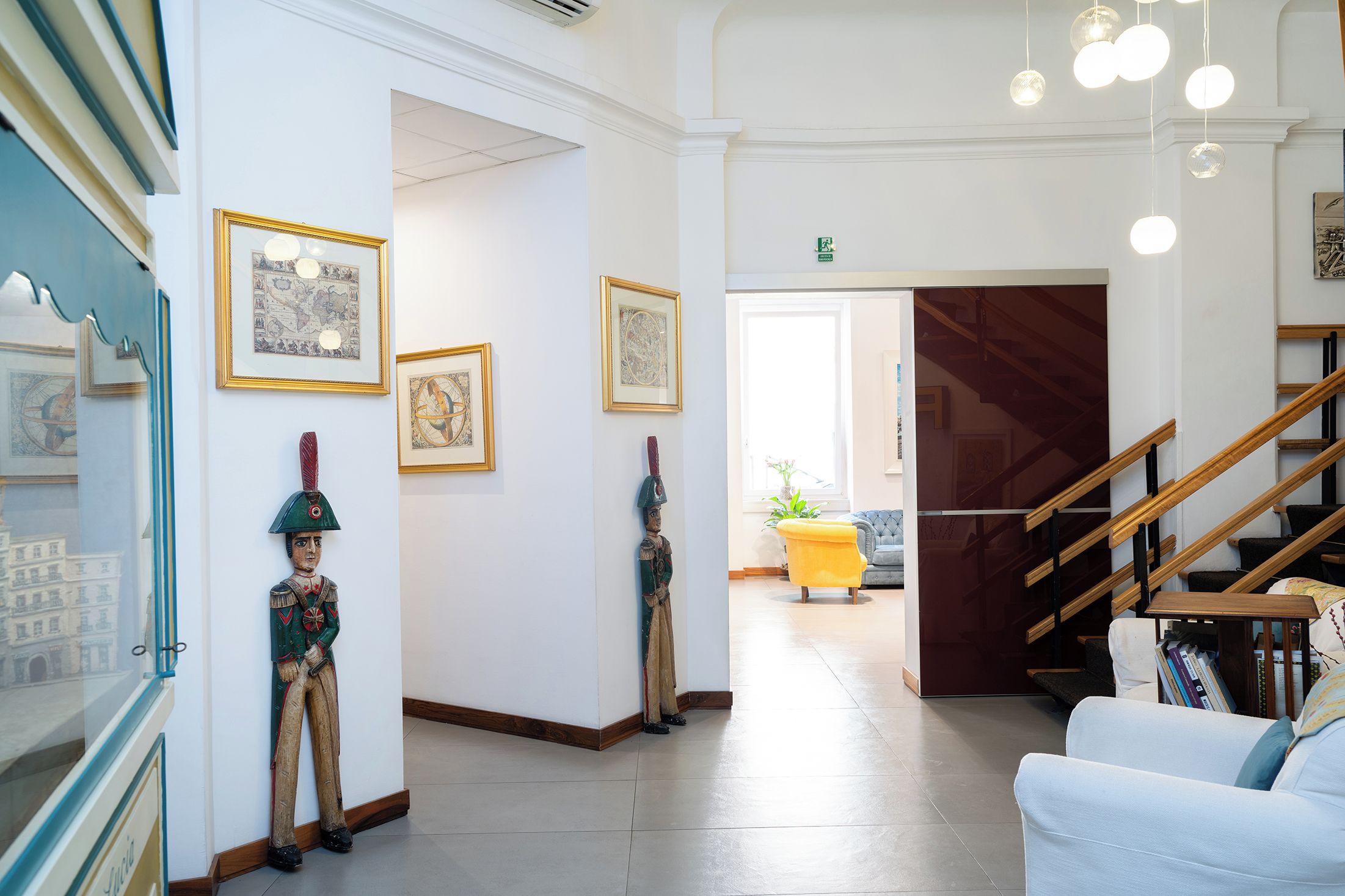 Corredor com obras de arte emolduradas, escada e área de estar com um banquinho amarelo.