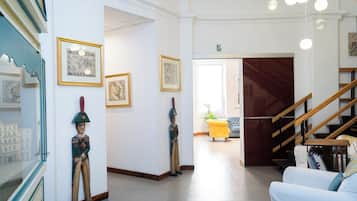 Corredor com obras de arte emolduradas, escada e área de estar com um banquinho amarelo.