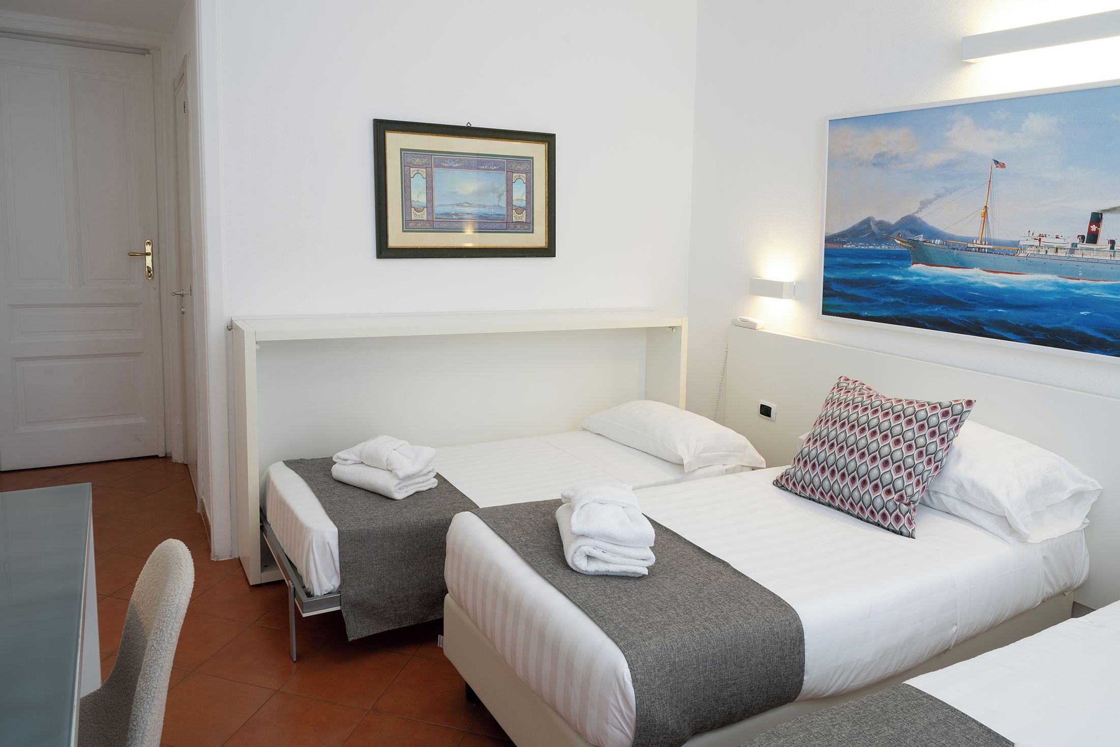 A hotel room with two beds, a painting on the wall, and a view of the sea.