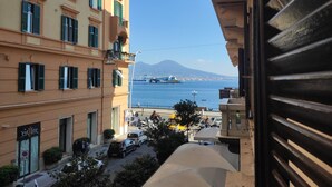 Une vue depuis un balcon donnant sur une rue où sont garées des voitures et sur un immeuble aux volets verts.