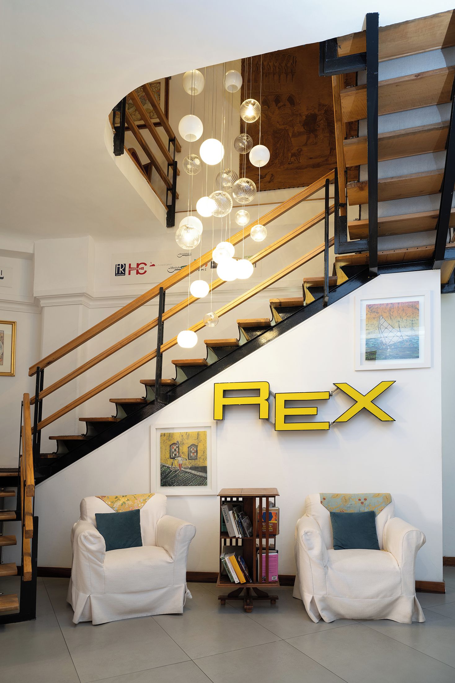 A modern interior with a curved staircase, white armchairs, and a bookshelf.
