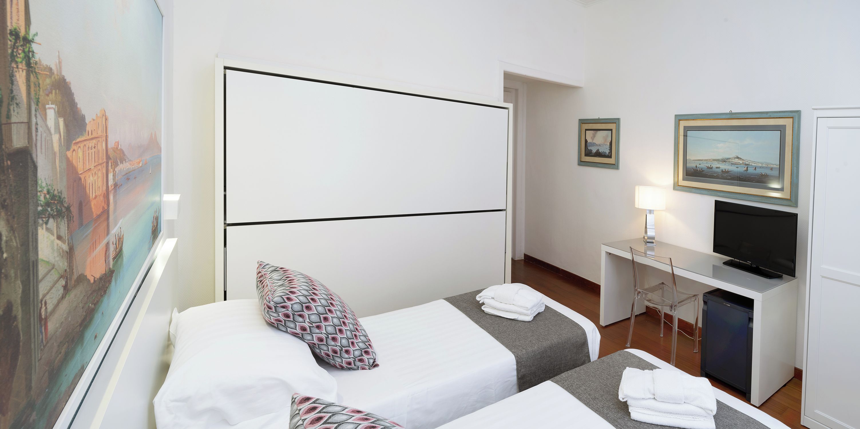Ein Hotelzimmer mit zwei Betten, einem Schreibtisch mit Fernseher und einem Bild an der Wand.