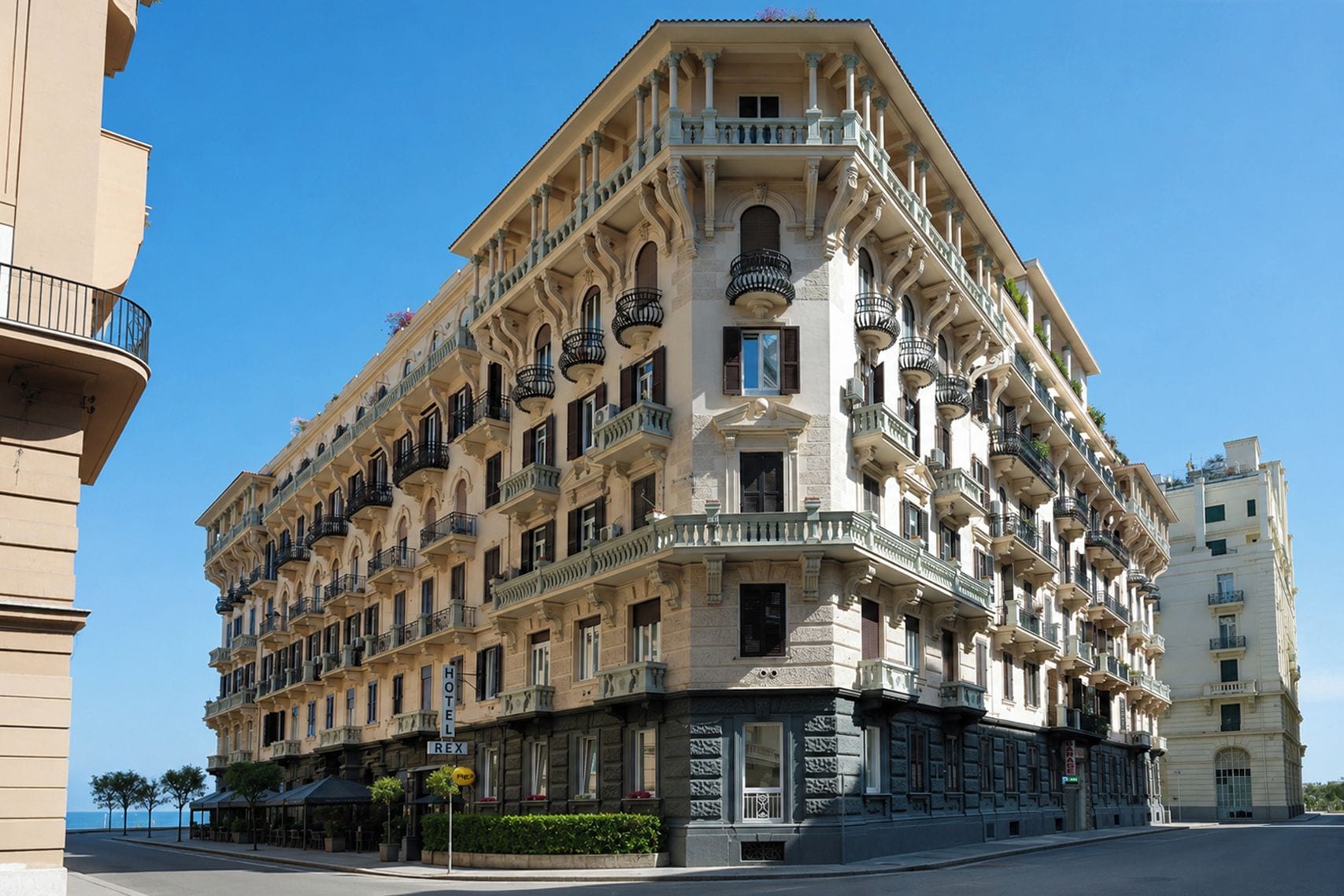 Un hotel de varios pisos con fachada en esquina, balcones y vista a la calle.
