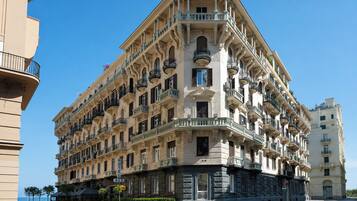 Un hotel de varios pisos con fachada en esquina, balcones y vista a la calle.