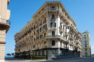 A multi-story hotel with a corner facade, balconies, and a street view.