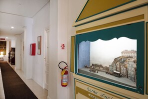 A hallway with a fire extinguisher mounted on the wall, a framed painting of a historical scene, and a sign indicating the location as 'Santa Lucia'. - Rex Lifestyle Hotel (Naples)