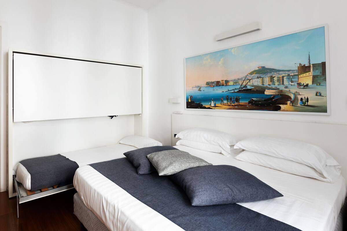 A hotel room with a large bed, two bedside tables, and a painting of a coastal scene on the wall.