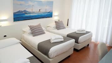 Une chambre d’hôtel avec deux lits, un tableau représentant un navire accroché au mur et une vue sur la mer.