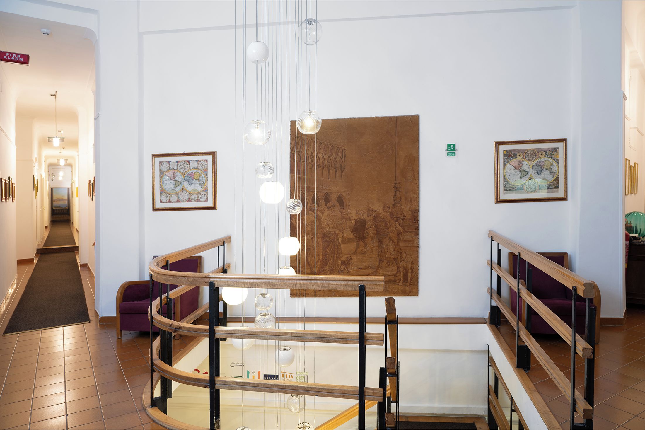 A hotel lobby with a staircase, a fire alarm sign, and framed artwork on the walls.
