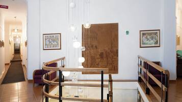 A hotel lobby with a staircase, a fire alarm sign, and framed artwork on the walls.