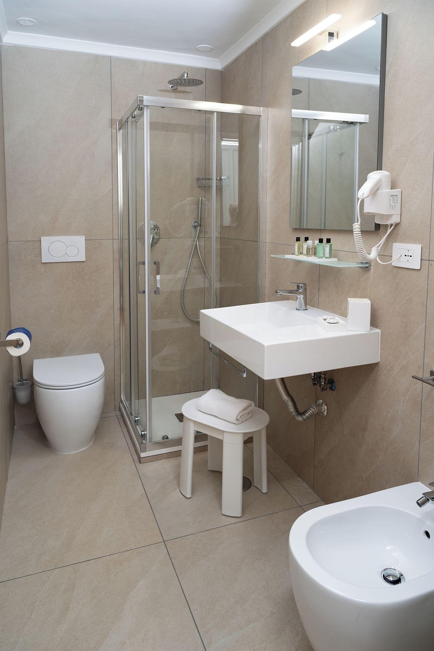 A modern bathroom with a glass-enclosed shower, a white sink, a toilet, and a bidet.